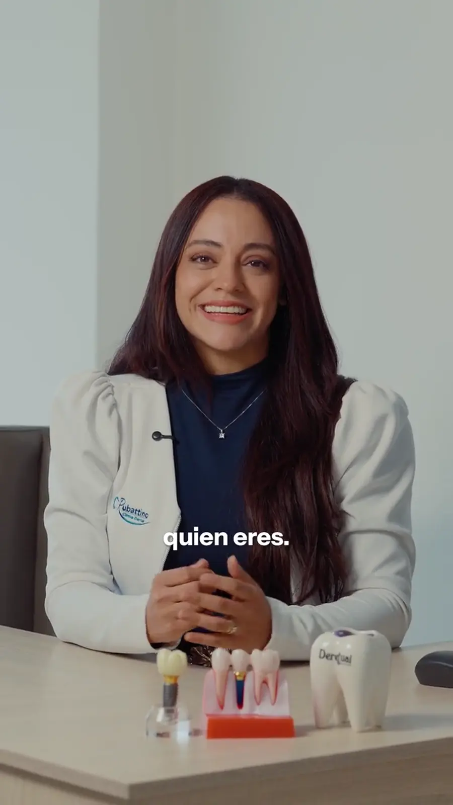 La Dra. Kim Rubattino, con su bata de la clínica, sonríe en su escritorio junto a modelos dentales.